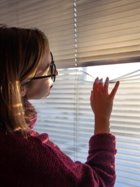 woman-looks-through-blinds-early-morning-sunlight_169016-17901